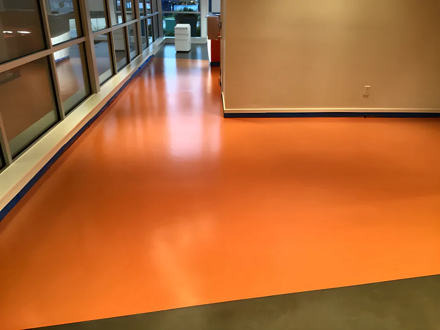 Pumpkin-orange urethane floor in a Whistler commercial interior, running along the glazed partitions and stopping clean at the grey concrete