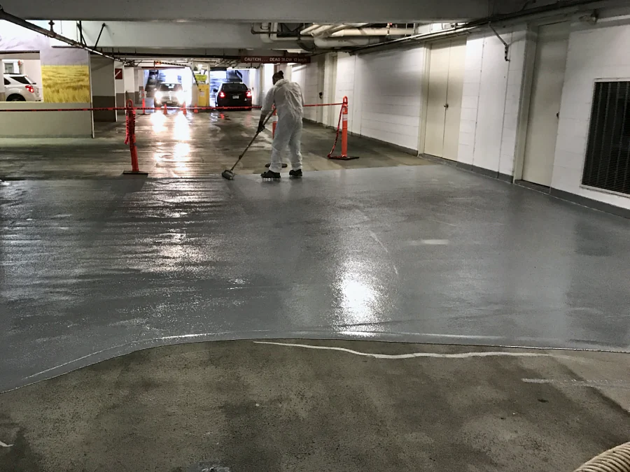 A crew member laying the new grey coat over the prepared deck of the Whole Foods parkade in Vancouver, the work taped off from the entrance