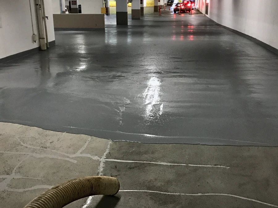 The leading edge of the new grey coat over the shot-blasted concrete of the Whole Foods parkade in Vancouver, its cracks filled in white